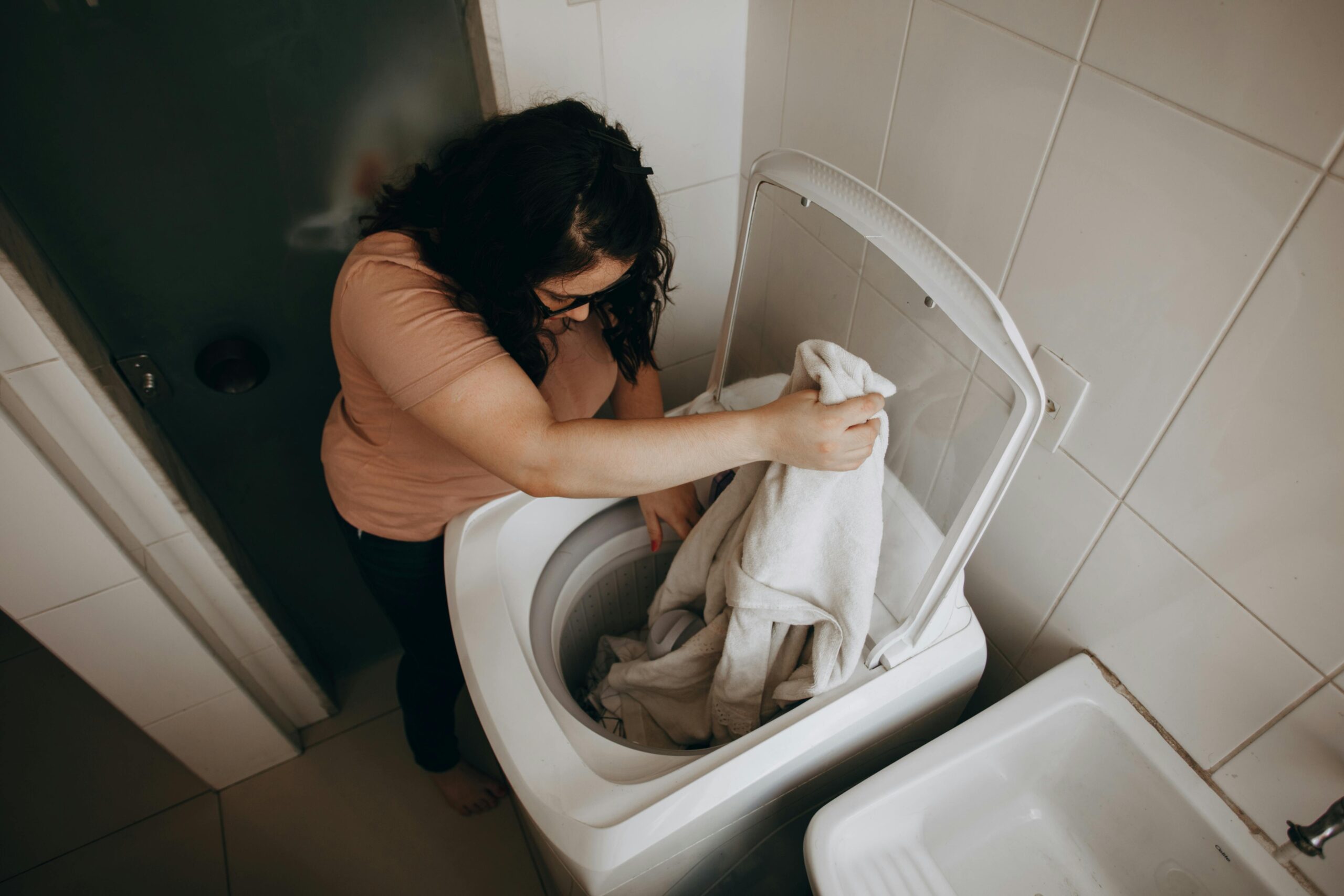 An adult woman loading clothes into a washing machine in a modern indoor space.